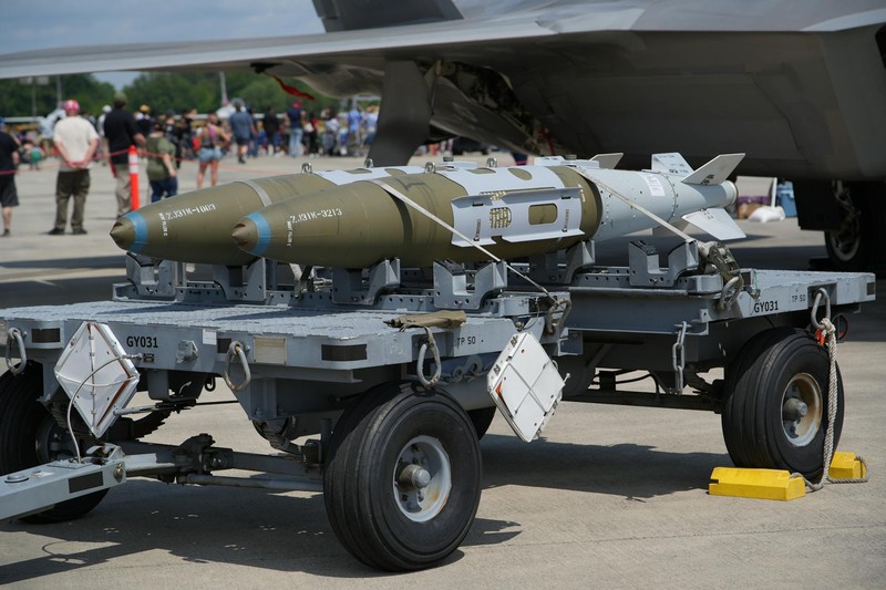 Close-up of a military bomb mounted on a transport cart beneath a fighter jet at an airshow
