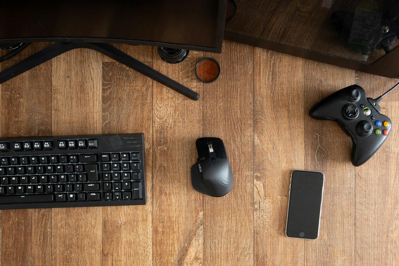 Top-down view of a gaming desk with keyboard, mouse, gamepad, and monitor on a wooden surface