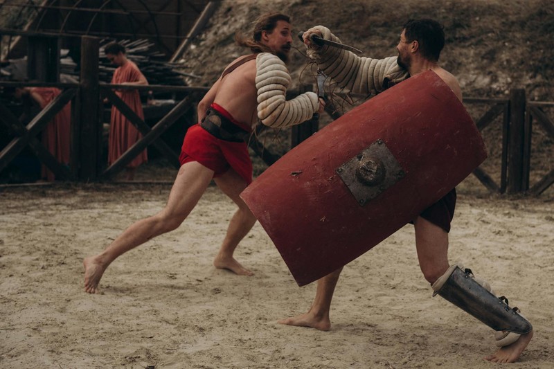 Two gladiators engaged in combat in a sandy arena
