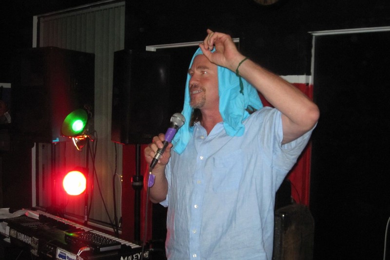 Val Kilmer performs with a microphone on a small stage at Pehrspace