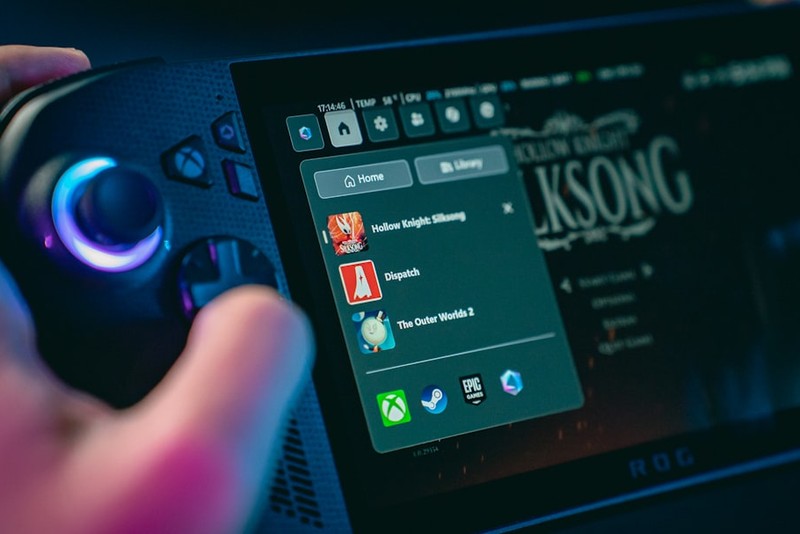 A handheld gaming console displaying a game library menu with titles listed on screen