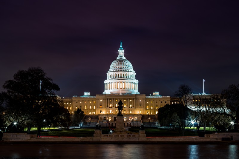 The United States Capitol illuminated at night, with its dome and facade reflected in the Capitol Reflecting Pool