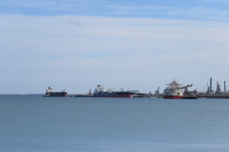 Oil tankers and bulk carrier docked at an oil refinery jetty with industrial infrastructure visible in the background