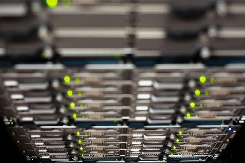 Server racks with green LED indicators in a modern data center, viewed at an angle with shallow depth of field