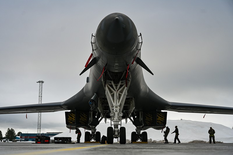 A U.S. Air Force B-1B Lancer strategic bomber parked on a wet tarmac under overcast skies with ground crew conducting maintenance