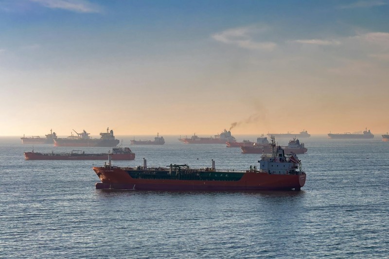 Oil tankers and cargo ships navigate a busy waterway at sunset