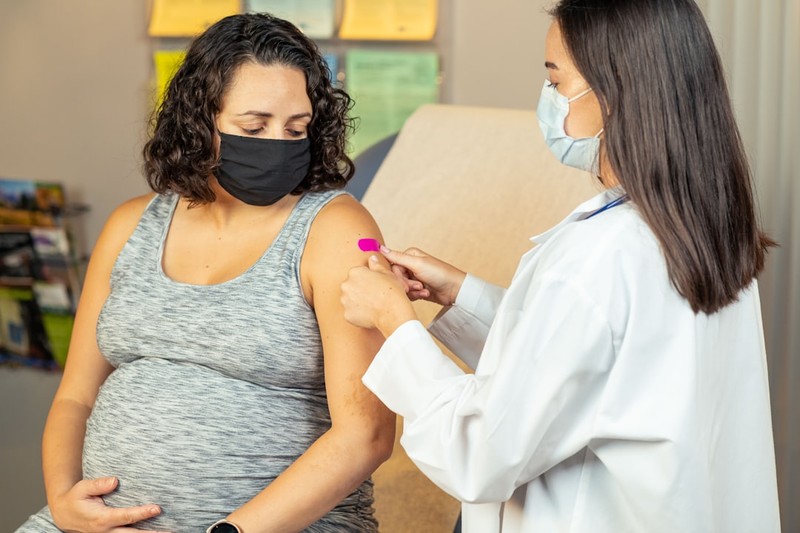 A healthcare provider administers a vaccine to a pregnant patient in a clinical setting