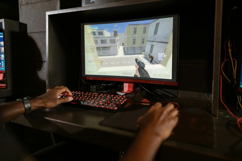 A person plays a first-person shooter video game on a gaming PC with a backlit keyboard