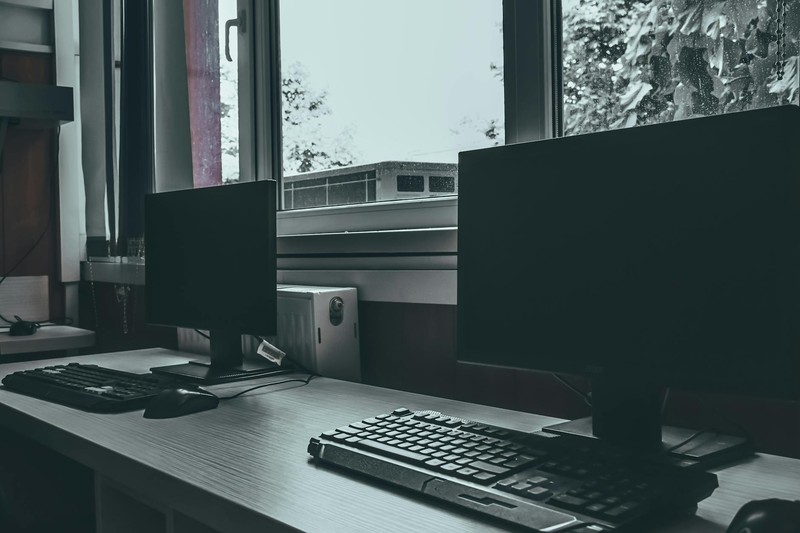 Empty desks with dark computer monitors in a dimly lit workspace, no one present