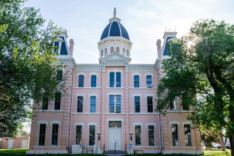 A stately historic courthouse with a blue domed roof and pink facade, framed by green trees under a clear sky
