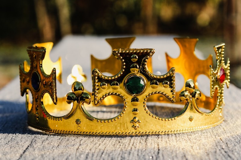 An ornate golden crown with gemstones resting on a weathered wooden surface