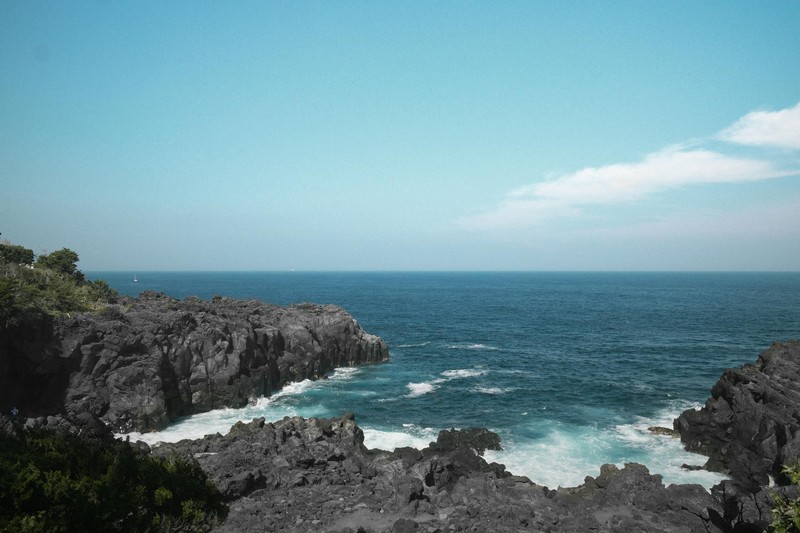 Dramatic rocky cliffs along Japan's coast with crashing ocean waves under a cloudy sky