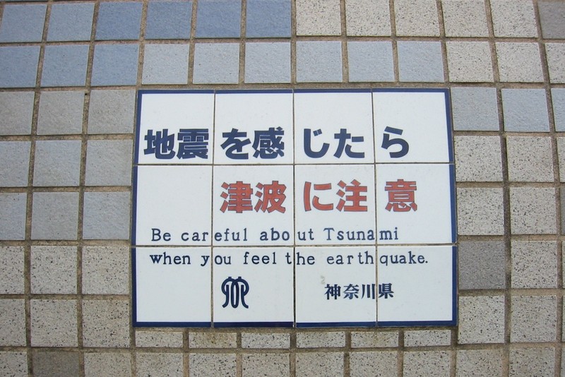 Bilingual tsunami warning sign mounted on a tiled seawall in Kamakura, Kanagawa Prefecture, Japan