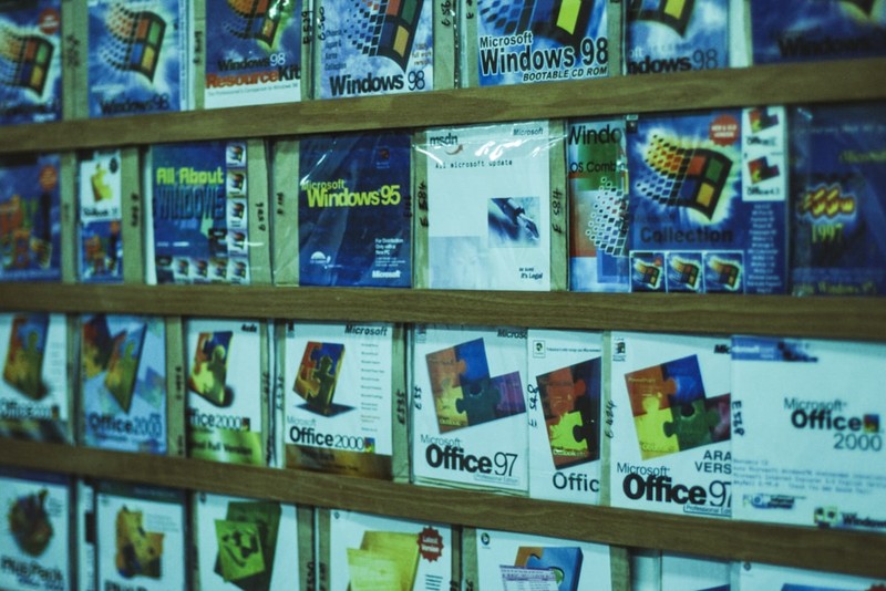 A wooden shelf displaying vintage Microsoft software boxes including Windows 95, Windows 98, and Microsoft Office 97 and 2000
