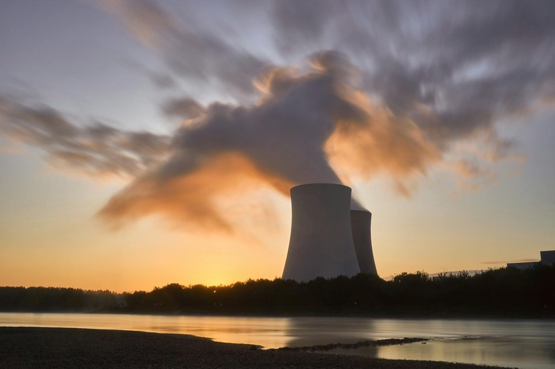 Nuclear power plant cooling towers at sunset with steam rising into a dramatic sky