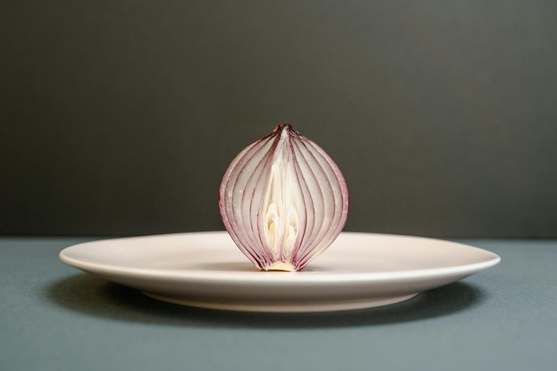 A half-sliced red onion displayed on a white plate against a dark backdrop