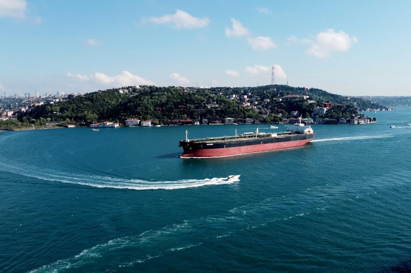 A cargo ship navigates through a narrow strait with a cityscape in the background, illustrating strategic maritime trade routes.