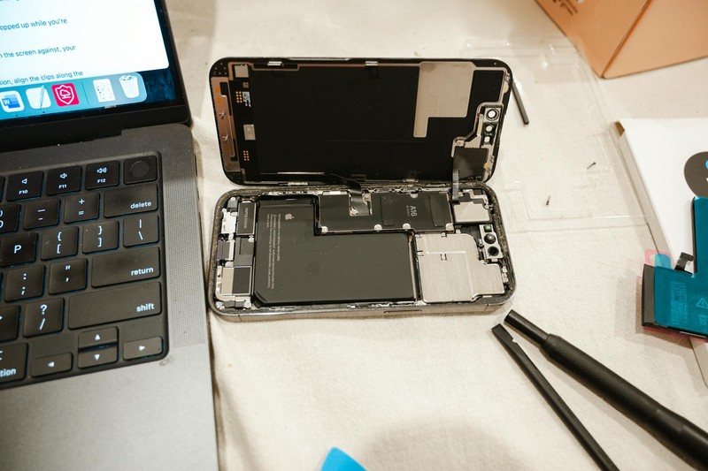 Disassembled smartphone with exposed battery and precision repair tools on a workbench