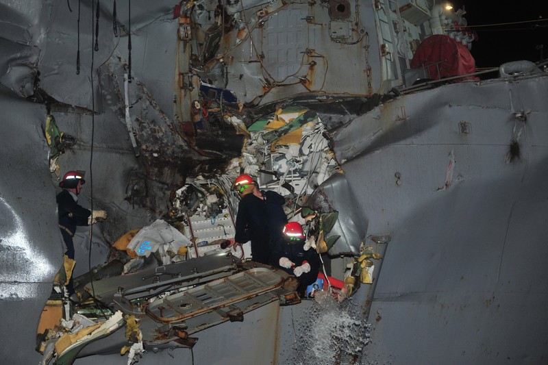 A damaged US Navy guided-missile destroyer in the Strait of Hormuz, with personnel inspecting the hull at night