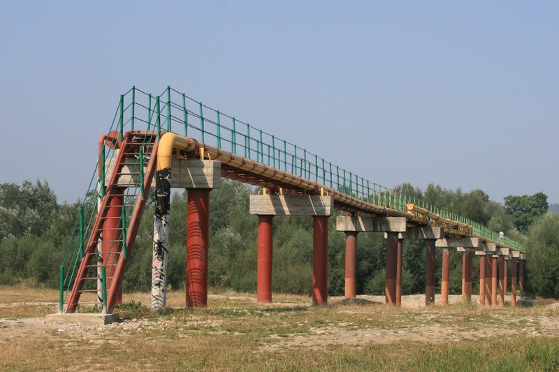 Elevated section of the Druzhba oil pipeline supported by red pillars stretching across a rural landscape