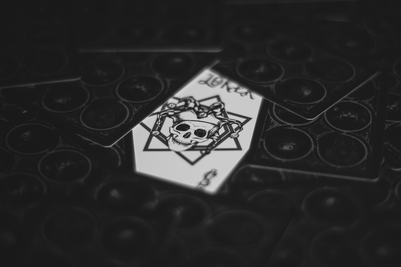 A Joker playing card with a skull jester design surrounded by face-down cards on a dark surface