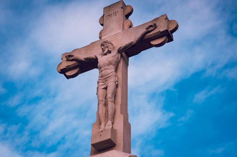 A stone statue of Jesus Christ on the cross against a clear blue sky