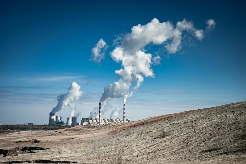 Industrial coal-fired power plant with smokestacks emitting thick white smoke against a clear blue sky