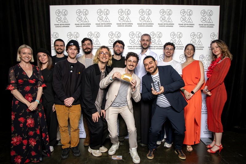 The Sandfall Interactive development team poses together at a GCA awards event, with some members holding trophies