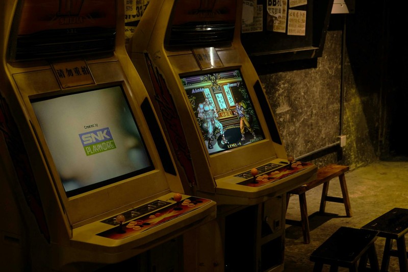Two vintage SNK arcade cabinets in a dimly lit retro arcade space with wooden stools