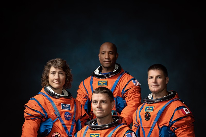 The four Artemis II crew members pose in their orange flight suits for an official portrait against a dark blue background