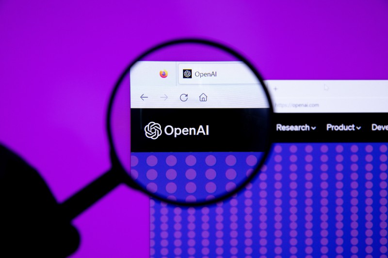 A magnifying glass focuses on the OpenAI logo on a webpage, symbolizing scrutiny of the company