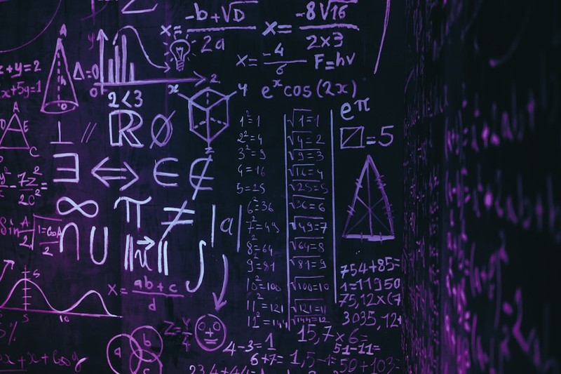 Mathematical formulas and equations written in purple chalk on a dark blackboard