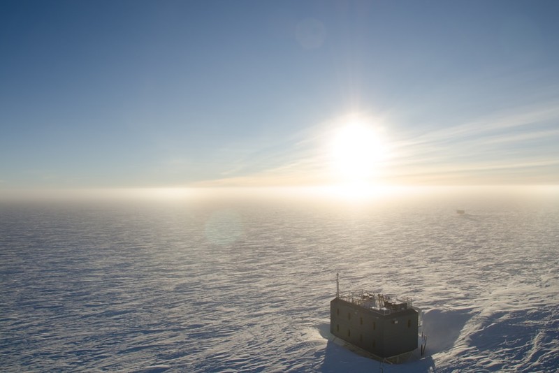 A research structure at South Pole Station on the vast Antarctic ice sheet, with the sun low on the horizon