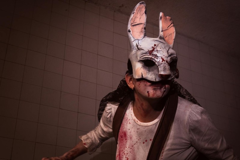 A person wearing a bloodstained horror rabbit mask in dim lighting