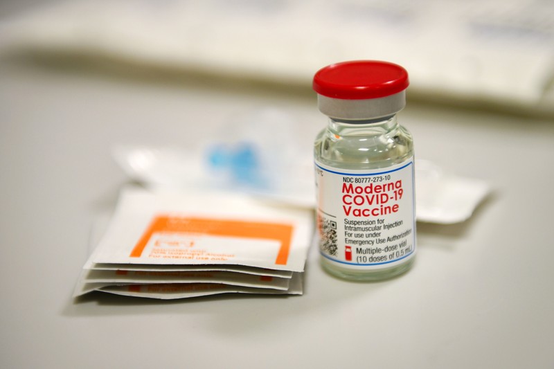 A Moderna COVID-19 vaccine vial with red cap alongside medical preparation supplies on a clinical surface
