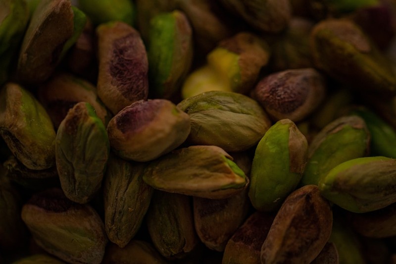 Close-up of pistachio nuts in their shells, showing natural texture and earthy green and brown tones.