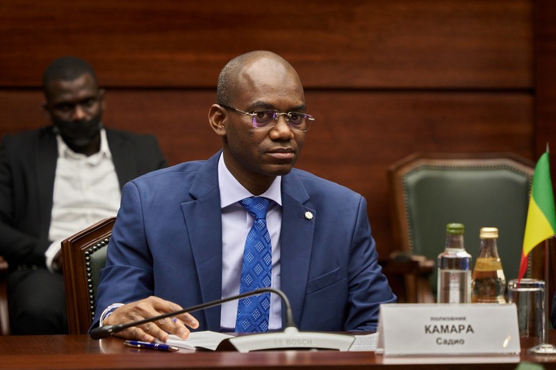 Mali's Defence Minister Sadio Camara seated at a formal meeting table in a wood-paneled conference room