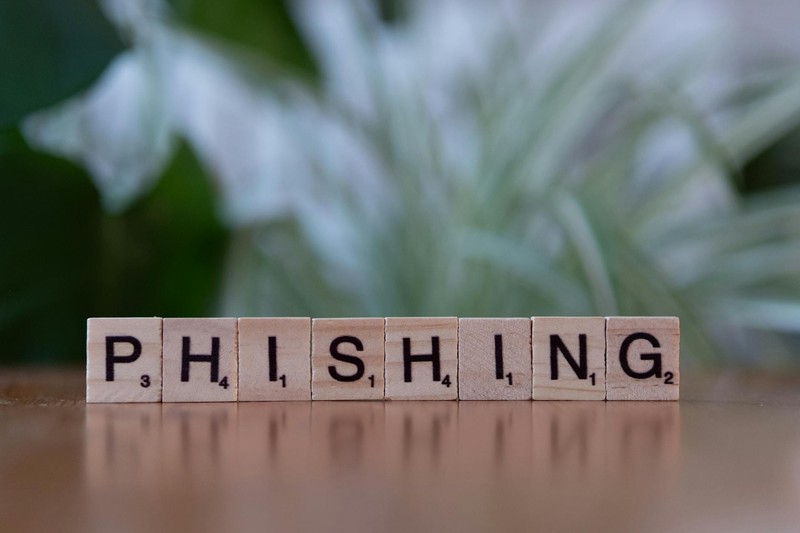 Wooden letter tiles spelling the word 'phishing' on a reflective surface with a blurred natural background.
