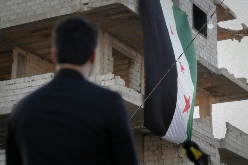 A person observes a Syrian flag draped over a war-damaged building in Damascus, Syria.
