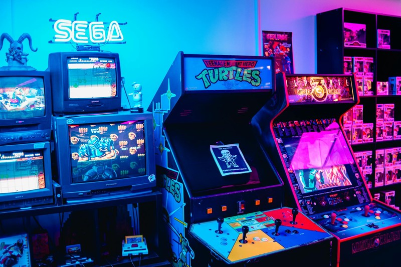 Neon-lit retro arcade room with classic arcade machines, CRT TVs, and colorful gaming collectibles