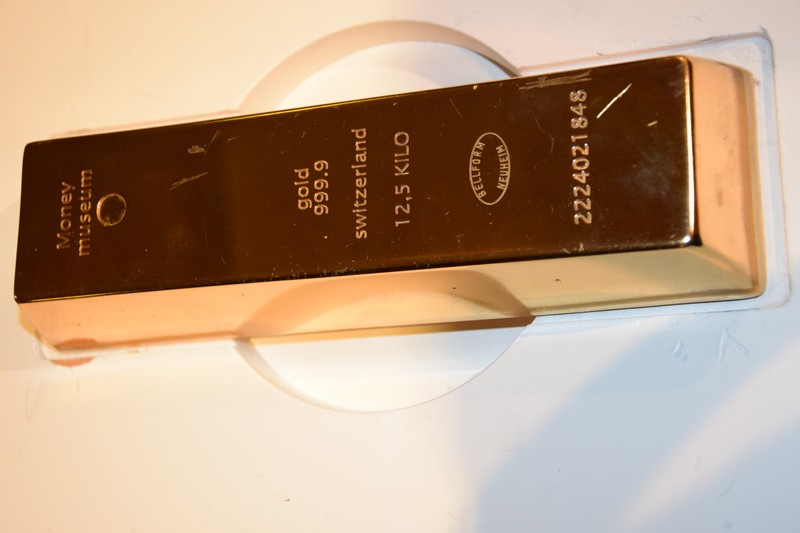 A large gold bullion bar displayed on a white stand, engraved with weight and purity markings