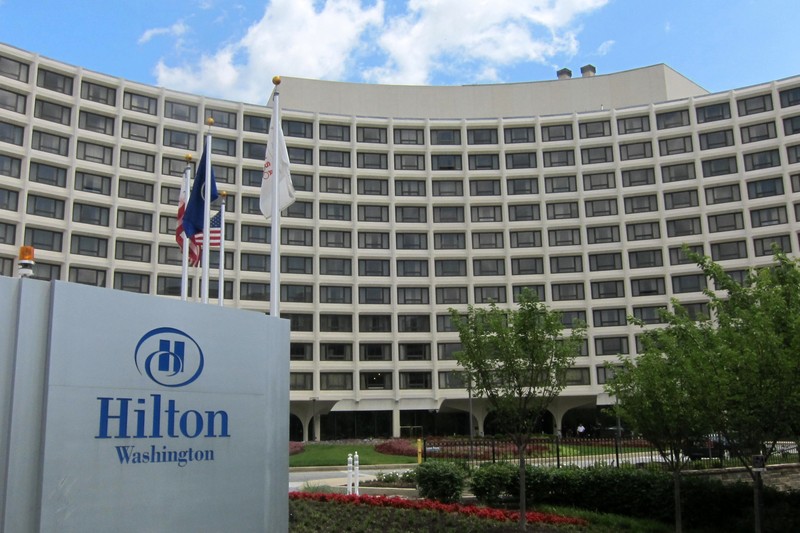 The Washington Hilton hotel building with its distinctive curved facade, American flags, and landscaped entrance