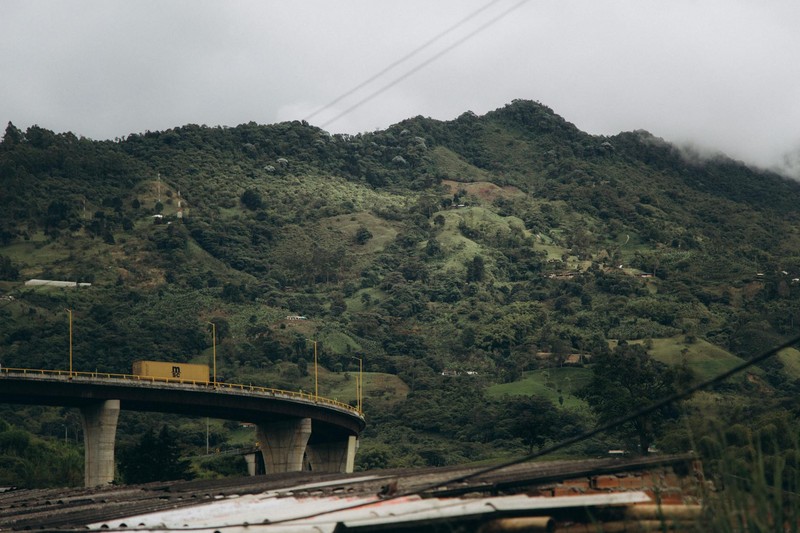 A highway bridge spanning a lush green mountain valley under an overcast sky