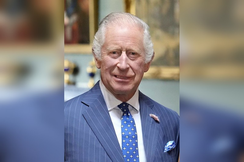 King Charles III in a formal diplomatic setting, wearing a dark suit with a composed expression