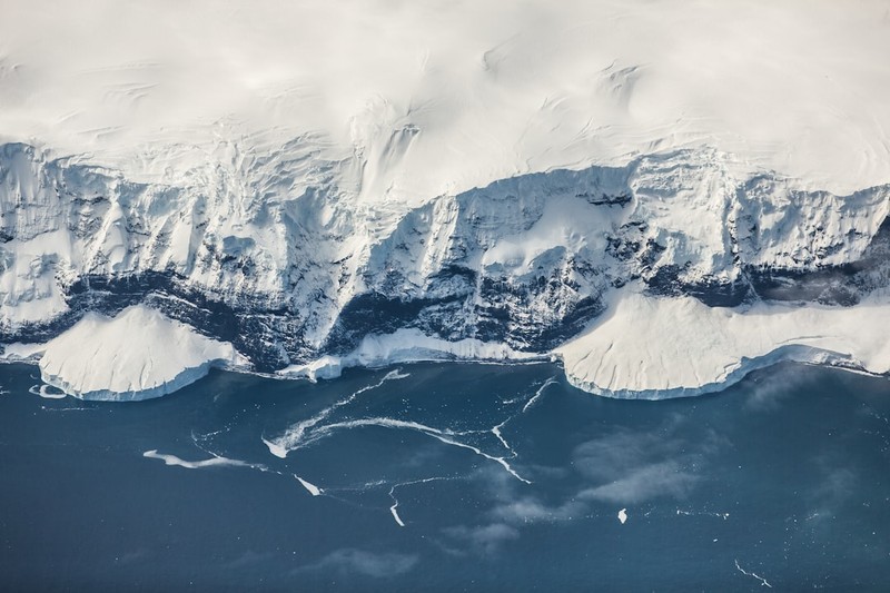 Aerial view of Antarctica's icy coastline meeting the deep blue Southern Ocean, with ice floes scattered in the water