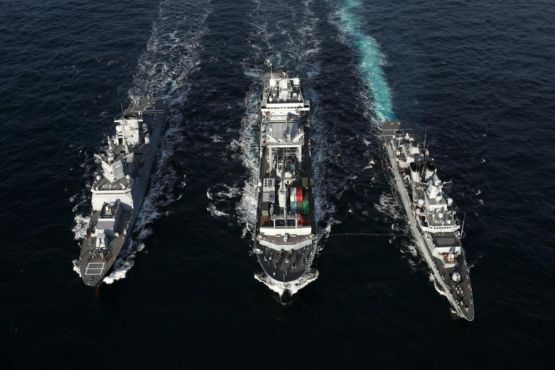 Three naval warships sailing in formation on open ocean, aerial view