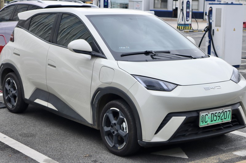 A white BYD electric vehicle parked at a charging station in Zhuhai, China, with a green EV license plate visible