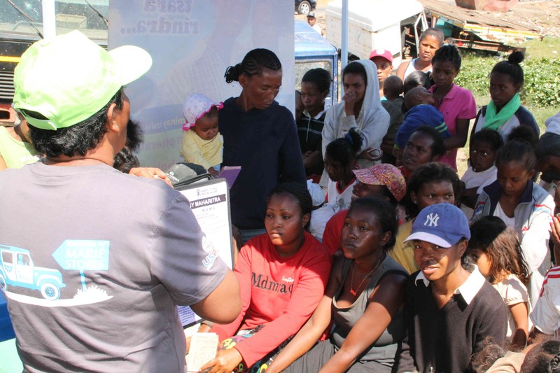 Women and children gather outdoors in Antananarivo, Madagascar, listening to a family planning presentation at a mobile clinic