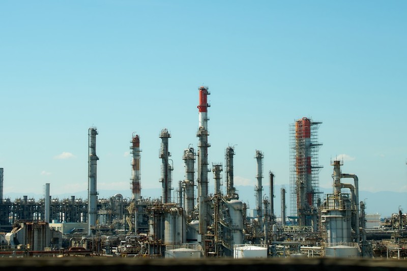 An industrial refinery with tall distillation towers and complex piping under a clear blue sky