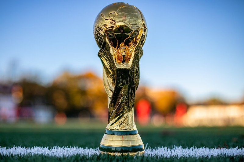 The FIFA World Cup trophy on a green soccer pitch with a blurred stadium background